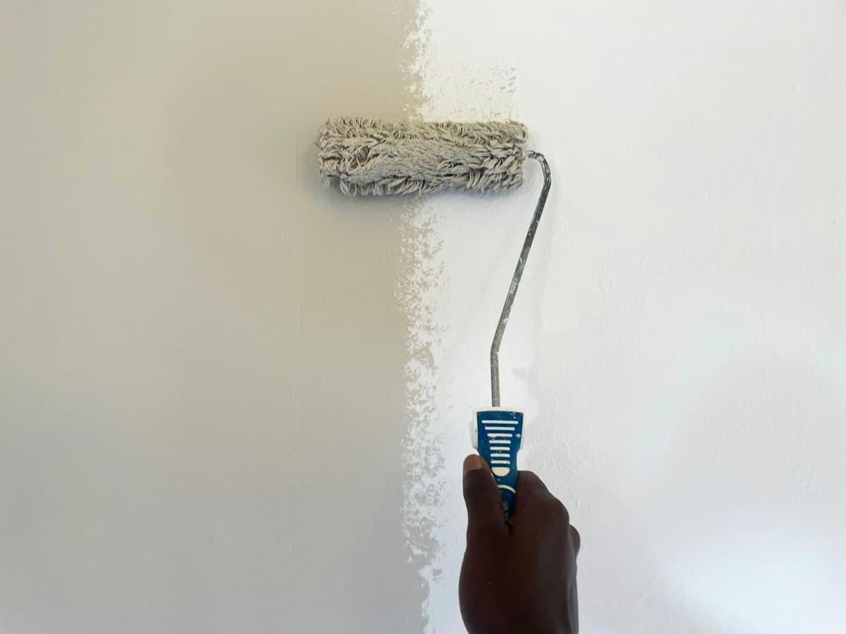 Hand mit Farbroller streicht eine helle Wand