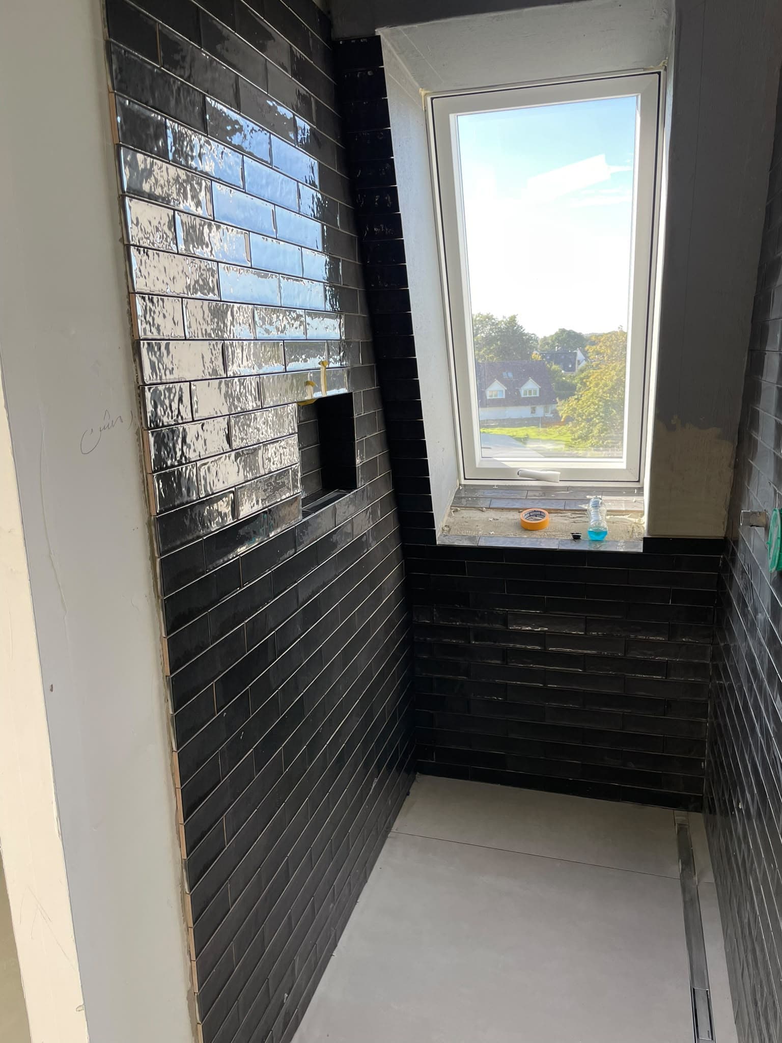 Dunkel geflieste Badezimmerwände neben einem Fenster