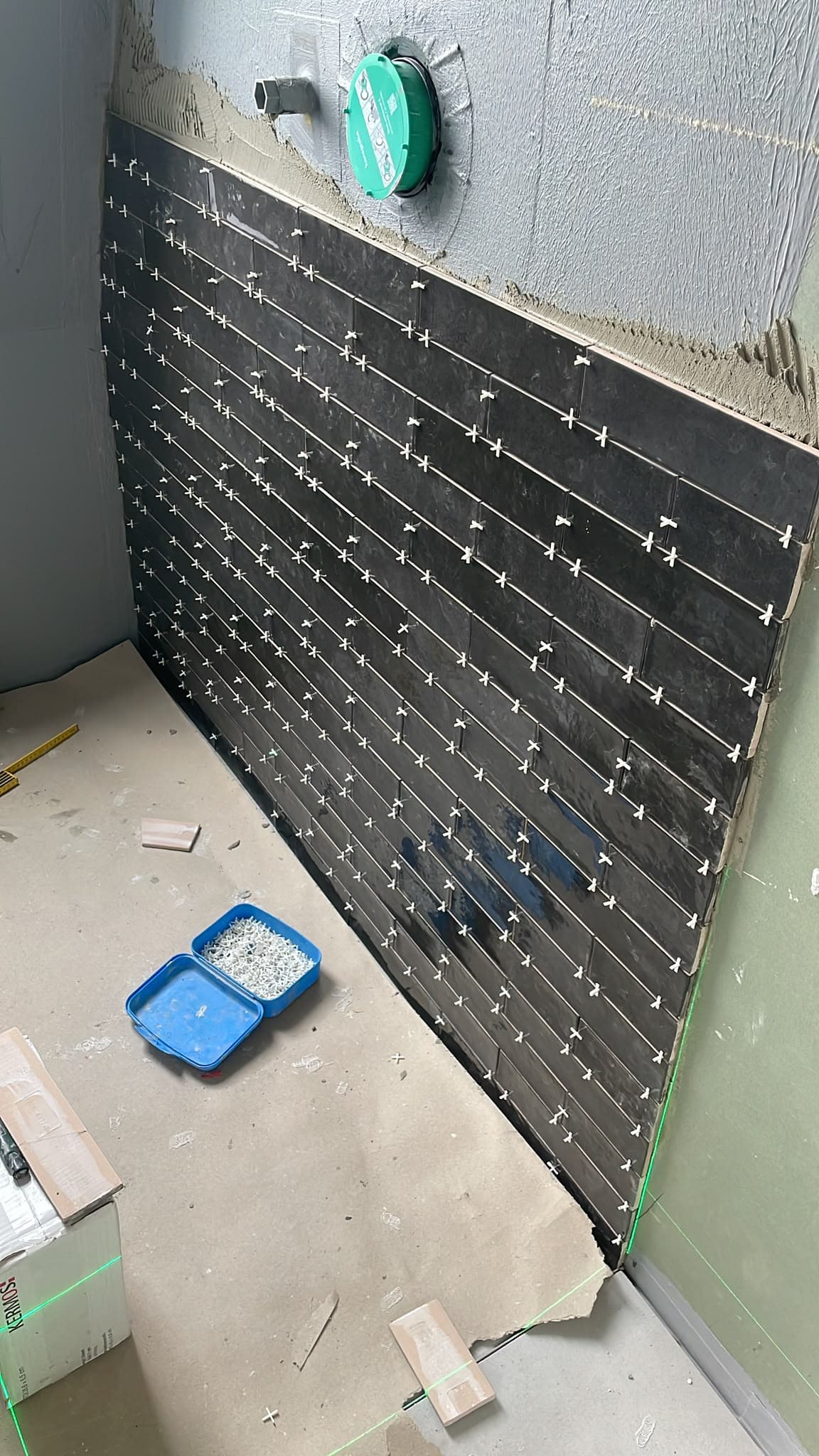 Dunkel geflieste Wand mit Abstandhaltern und Laserlinie